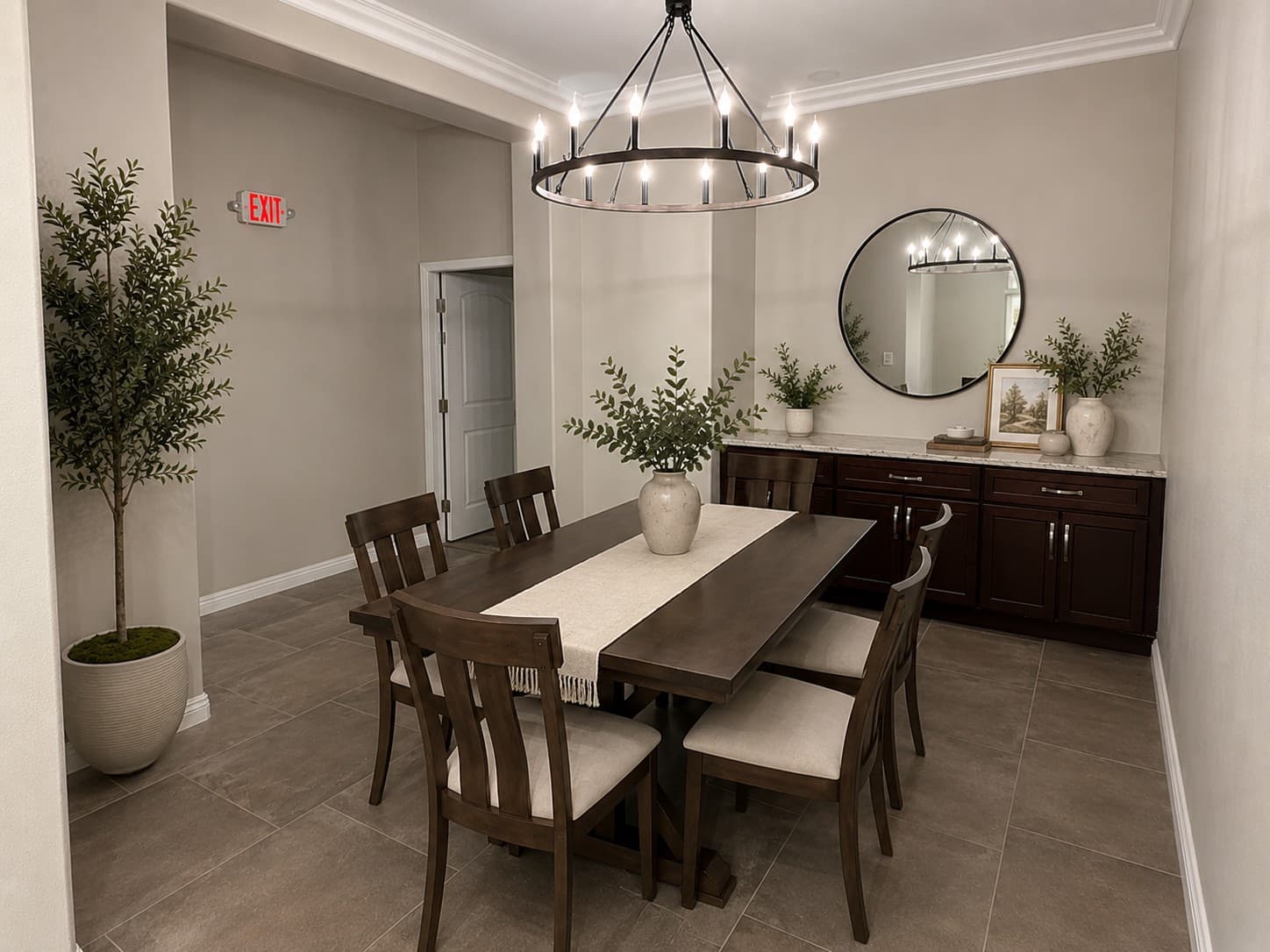 Dark wood dining table and chairs under a wagon-wheel chandelier in a neutral-toned room.